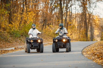 Man and woman driving quad bikes in autumn forest
