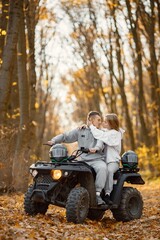 Man and woman kissing on a quad bike in autumn forest