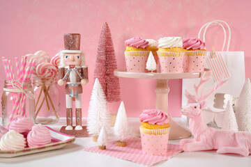 On trend pink Christmas children's party table with cupcakes, pink nutcracker, reindeer, mini trees, and decorations.
