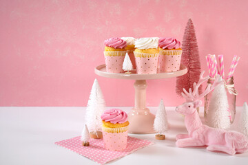 On trend pink Christmas children's party table with cupcakes, pink nutcracker, reindeer, mini trees, and decorations. Cupcakes on cake stand with copy space.