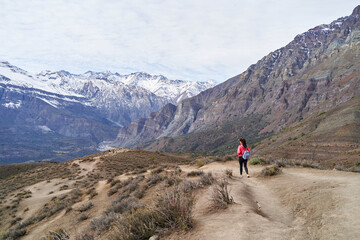 young woman with red jacket and backpack, descending the mountain in the middle of the Andes...