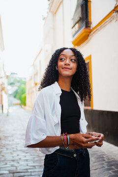 Cheerful African Woman Listening To Music On Wireless Ear Buds And Holding The Charging Case