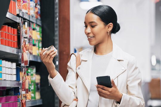 Supermarket, shopping and customer with smartphone check price, label or product information online. Retail consumer woman with food or grocery checking discount code or sales choice on a digital app