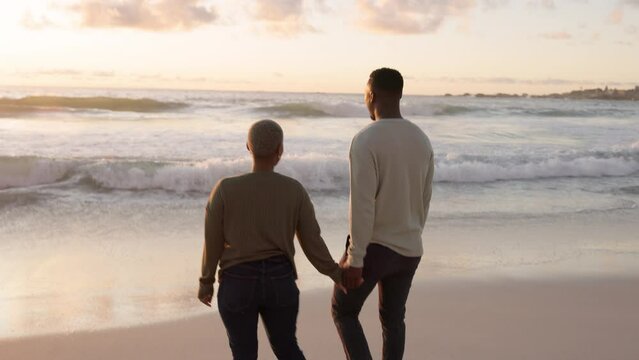 Beach, love and happy couple walking in the ocean while holding hands on a romantic date. Black man and woman enjoying nature and watching the sunset by sea water while on spring vacation together.