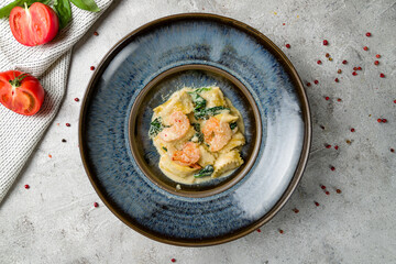 ravioli with shrimp and spinach on blue plate on grey table top view