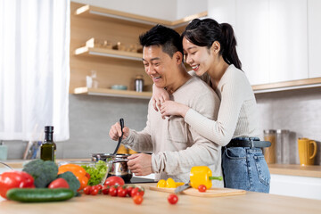 Happy young asian lady hugging her spouse cooking dinner