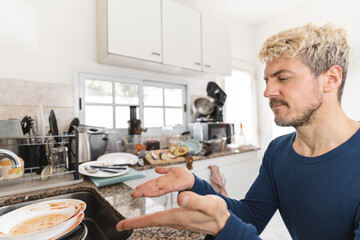 Mid-adult man complaining about dirty dishes in his messy kitchen