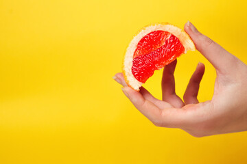 Defocus female hand holding piece of a red grapefruit. Healthy food concept.  Fresh orange juice. Vegan, vegetarian concept. Banner with copy space. Citrus fruit. Out of focus