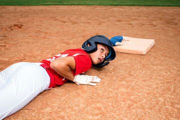 Teenage male baseball player sliding in the dirt to reach the base