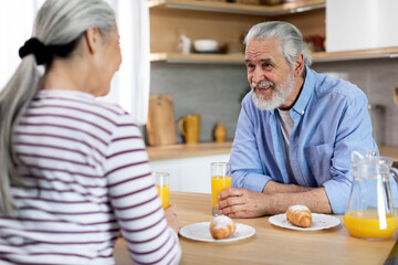 Senior Married Couple Chatting While Having Breakfast Together In Kitchen