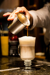Serving coffee cappuccino into a glass cup on a coffe bar