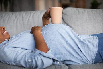 Obraz premium Unrecognizable Pregnant Black Female Holding Cup Lying On Sofa Indoor