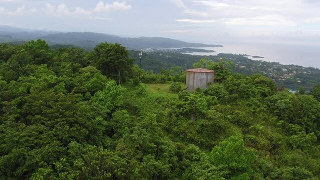 Aerial view rising over the crest of a the Drapers hillside to reveal Port Antonio in the distance with navy island as the camera continues to pan down onto the valley below