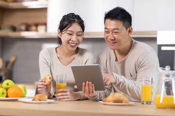 Smiling chinese spouses having breakfast and using tablet