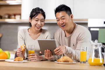 Obraz na płótnie Canvas Cheerful asian family using digital tablet while having breakfast