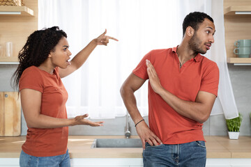 Upset angry millennial african american wife screaming scolding offended husband in kitchen interior