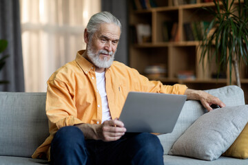 Happy senior man using modern laptop at home