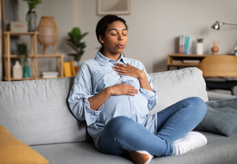 Pregnant African American Woman Doing Breathing Exercise Sitting At Home