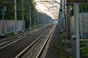 Empty railway tracks with green light semaphore at sunset, forest on background. Perspective of...