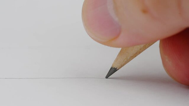 Macro of pencil writing or drawing. Unknown person drawing line or letter on white paper.
