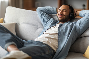 Smiling African American Guy Listening Music While Relaxing On Couch At Home