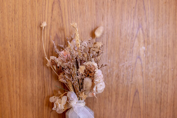 Dried flowers in a vase are placed in front of a wooden wall.