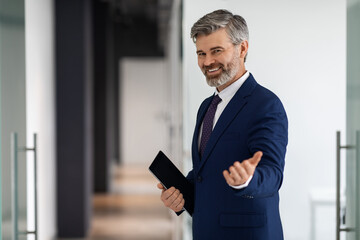 Handsome Middle Aged Businessman In Suit Making Inviting Gesture, Welcoming To Enter Office