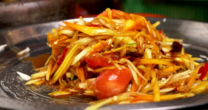 Close-up front view, Chef scooped the spicy green papaya salad or Som Tum onto the plate, Thai traditional street food. 