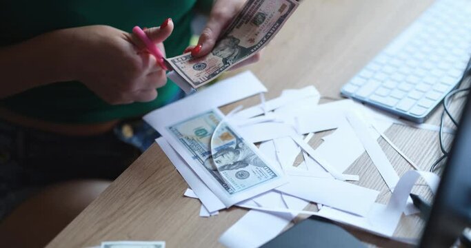 Counterfeiter woman cuts dollar bills with scissors at table closeup