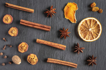 Fototapeta na wymiar There are dry circles of orange, cinnamon sticks, stars of star anise, cloves, nutmeg, pepper on a black background. Ingredients for mulled wine, a recipe for making a traditional warming drink