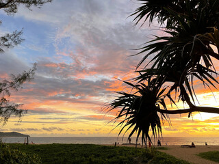 Beautiful sunset at the tropical beach. Amazing colorful sky with clouds and sun glow. Palm trees. People on the sand coast. Scenery photo. Seascape. Tropical paradise. Beauty of nature. Twilight.