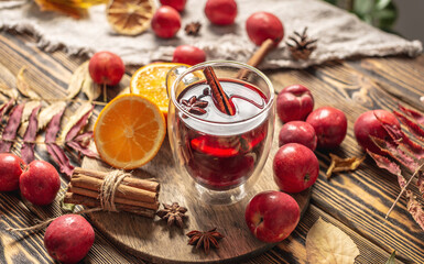 Glass cup with mulled wine decorated with cinnamon, star anise and orange on a wooden table. Concept of a traditional warming beverage