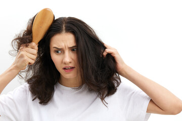 Fototapeta premium a sad, upset woman is trying to comb her long, dark, tangled hair with a wooden massage comb with a very sad, sad face