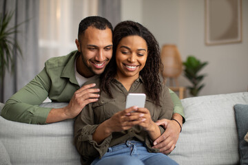 Happy Black Spouses Using Cellphone Texting At Home