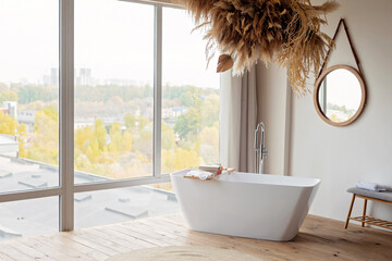 Comfortable bright bathroom with a boho-chic interior design, a free-standing white bath against...
