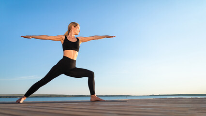 Fototapeta na wymiar Beautiful Middle Aged Woman Practicing Yoga Outdoors, Standing In Warrior Pose