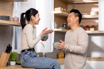Happy chinese couple drinking coffee together at kitchen