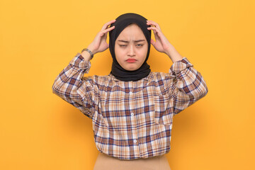 Doubtful young Asian woman in plaid shirt scratching head and trying to find solution isolated on yellow background