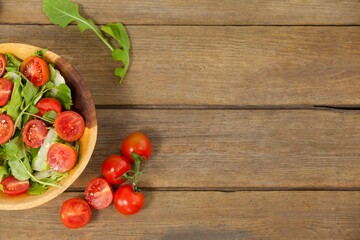 Fresh salad in bowl by tomatoes on wooden table