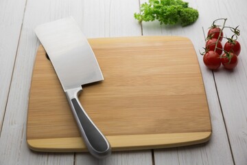 Knife on wooden chopping board with tomatoes and parsley