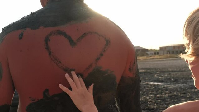 Children's hands close up. The child draws on the father's back. The girl draws a heart. The concept of love, father's day, fatherhood, valentine's day. Rays of the sun, love and jokes. Application of