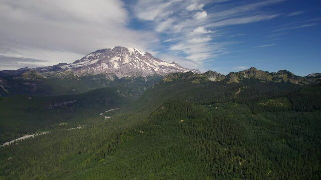Drone video taken over Gifford Pinchot National Forest of Mt. Rainier covered with snow under blue sky with a lenticular cloud formation.