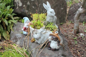 Garden statues gathered with potted plants on a rock