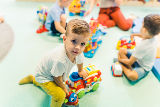 Imagination and Creativity development. Cognitive Growth. Toddlers boys and their nursery teacher playing with plastic toys and colorful car in a nursery school playroom. High quality photo