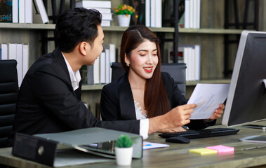 Millennial Asian young professional successful female businesswoman ceo entrepreneur in formal suit sitting smiling working via computer while male businessman secretary helping writing note on paper
