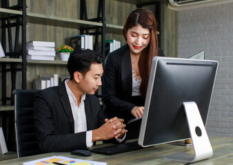 Millennial Asian young professional successful male businessman ceo entrepreneur in formal suit sitting looking reading checking paperwork document in folder from female businesswoman secretary
