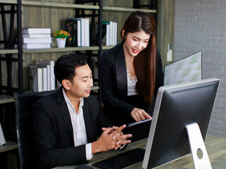 Millennial Asian young professional successful male businessman ceo entrepreneur in formal suit sitting looking reading checking paperwork document in folder from female businesswoman secretary