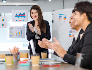 Asian young beautiful professional successful businesswoman presenter standing smiling in front of glass board after presenting while male female colleagues clapping hands thank you in meeting room