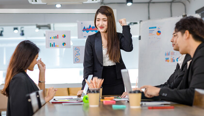 Asian young beautiful professional successful businesswoman presenter standing smiling in front of glass board after presenting while male female colleagues clapping hands thank you in meeting room