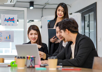 Asian young beautiful professional successful businesswoman mentor standing smiling pointing computer coaching teaching strategy to group of male and female businesspeople colleagues in meeting room